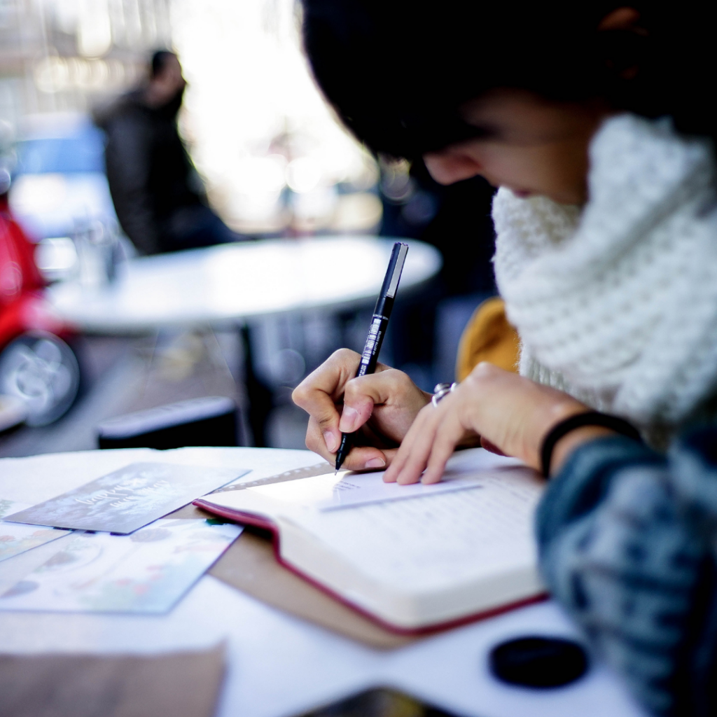 Frau mit Wollschal notiert Journaling-Ideen in einem Café