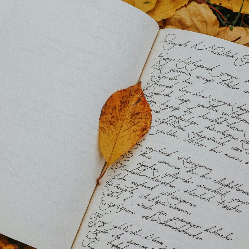Handschriftlich beschriebenes Notizbuch mit einem gelben Herbstblatt