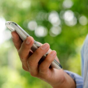 Hand hält ein Smartphone vor grünem Hintergrund – Bildschirmzeit bewusst reduzieren